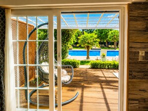 A glass door leading to a pool area with a hanging chair, a palm tree, and a wooden deck. - 216 North Hotel & Wellness-Spa (Sile)