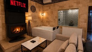 Una sala de estar acogedora con chimenea, un cartel de Netflix, una bañera moderna y una pared de piedra.