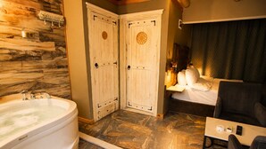 Un baño con una bañera grande, dos puertas de madera, una cama con cabecera y una mesita con un control remoto.