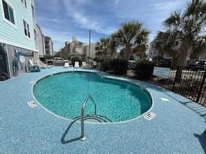 A pool with a lifeguard sign, palm trees, and a building in the background.