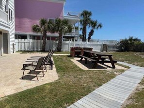 A patio area with picnic tables and a barbecue grill, surrounded by a white fence and palm trees. - Boston Commons 101 3 Bedroom Condo by RedAwning (Surfside Beach)