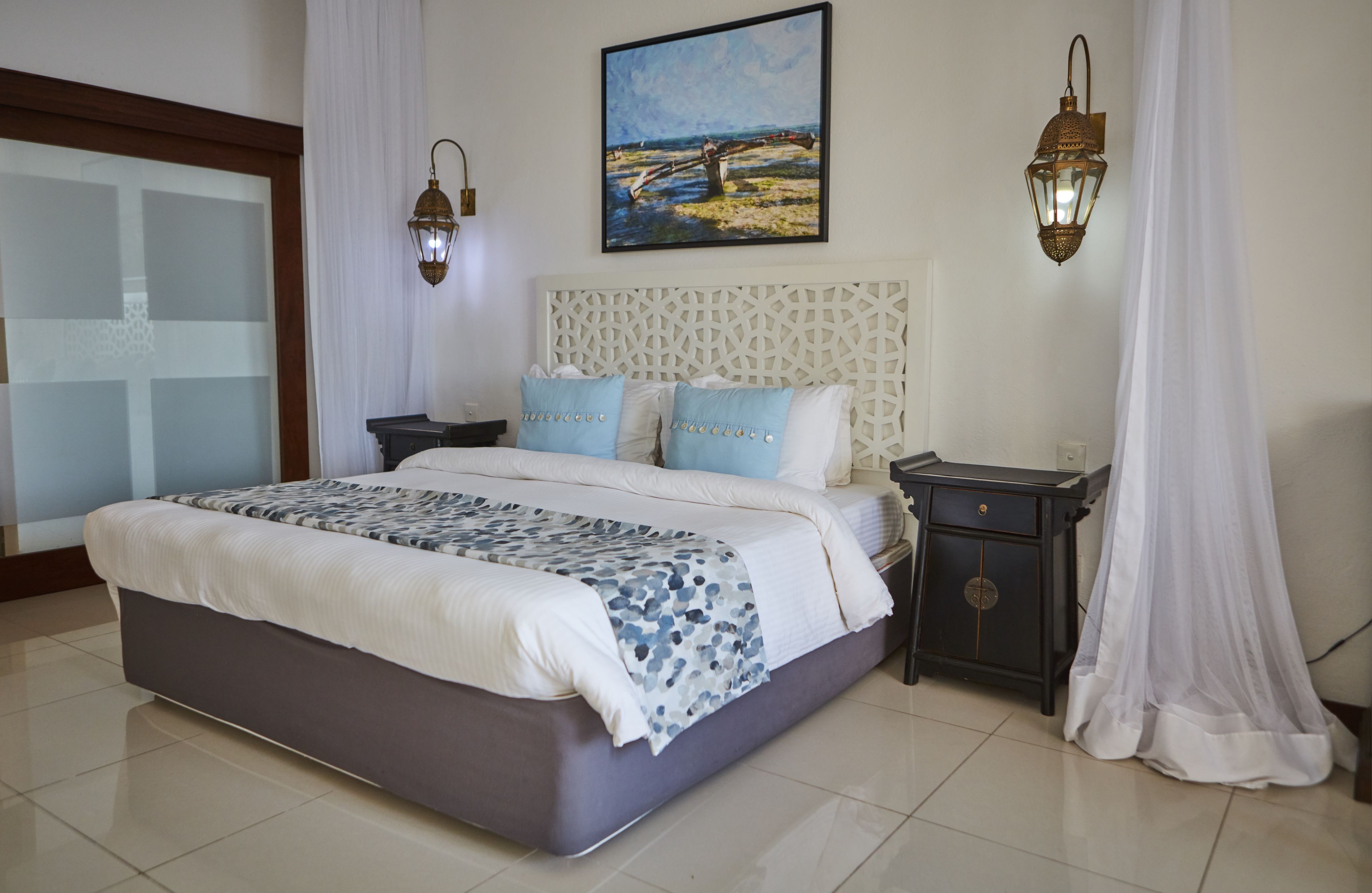 A bedroom with a bed, nightstands, a painting, and two wall-mounted lamps.