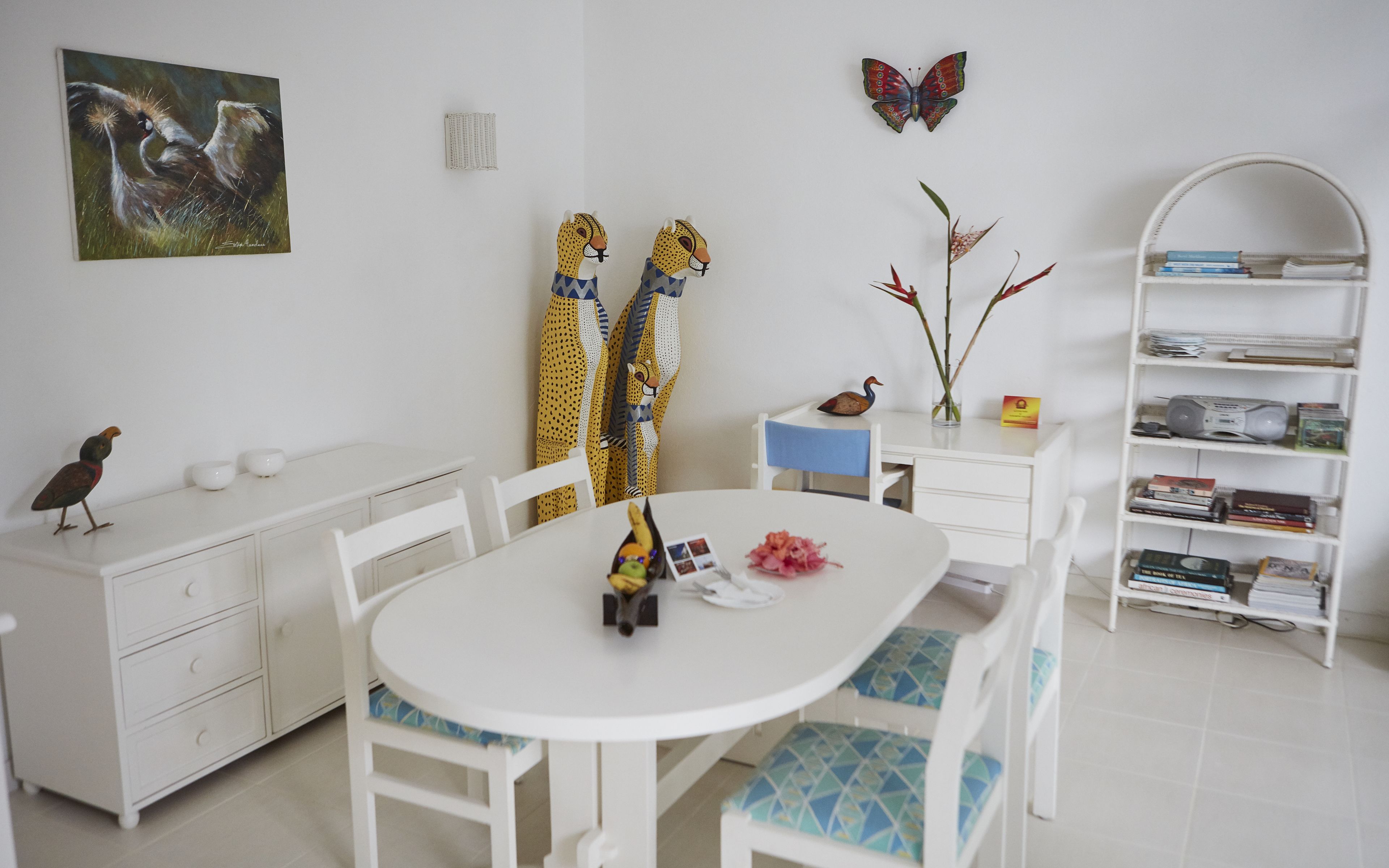 A modern, well-lit room with a white dining table, chairs, a bookshelf, and a butterfly decoration on the wall.