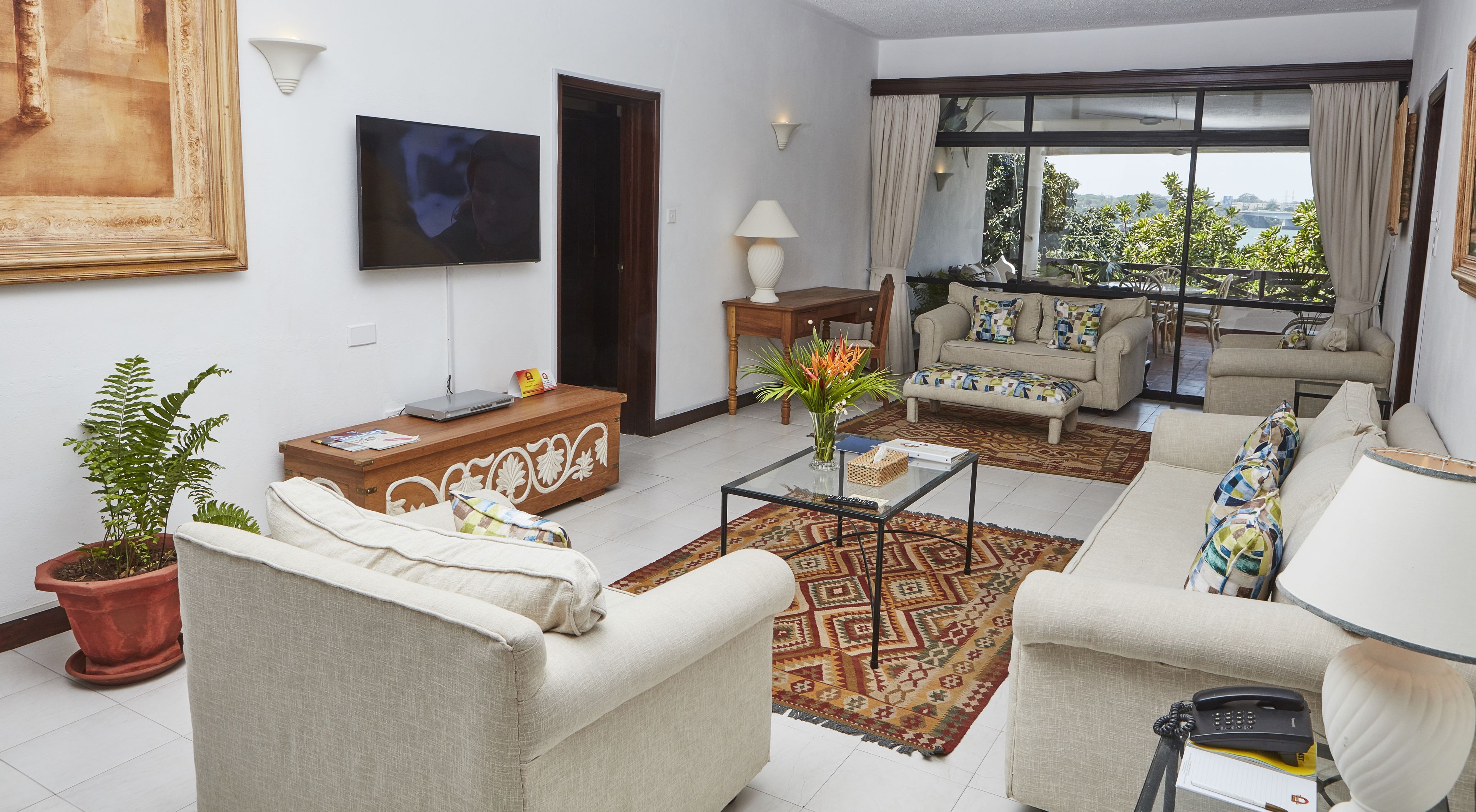 A living room with a sofa, armchairs, a coffee table, a TV, and a balcony with a view.