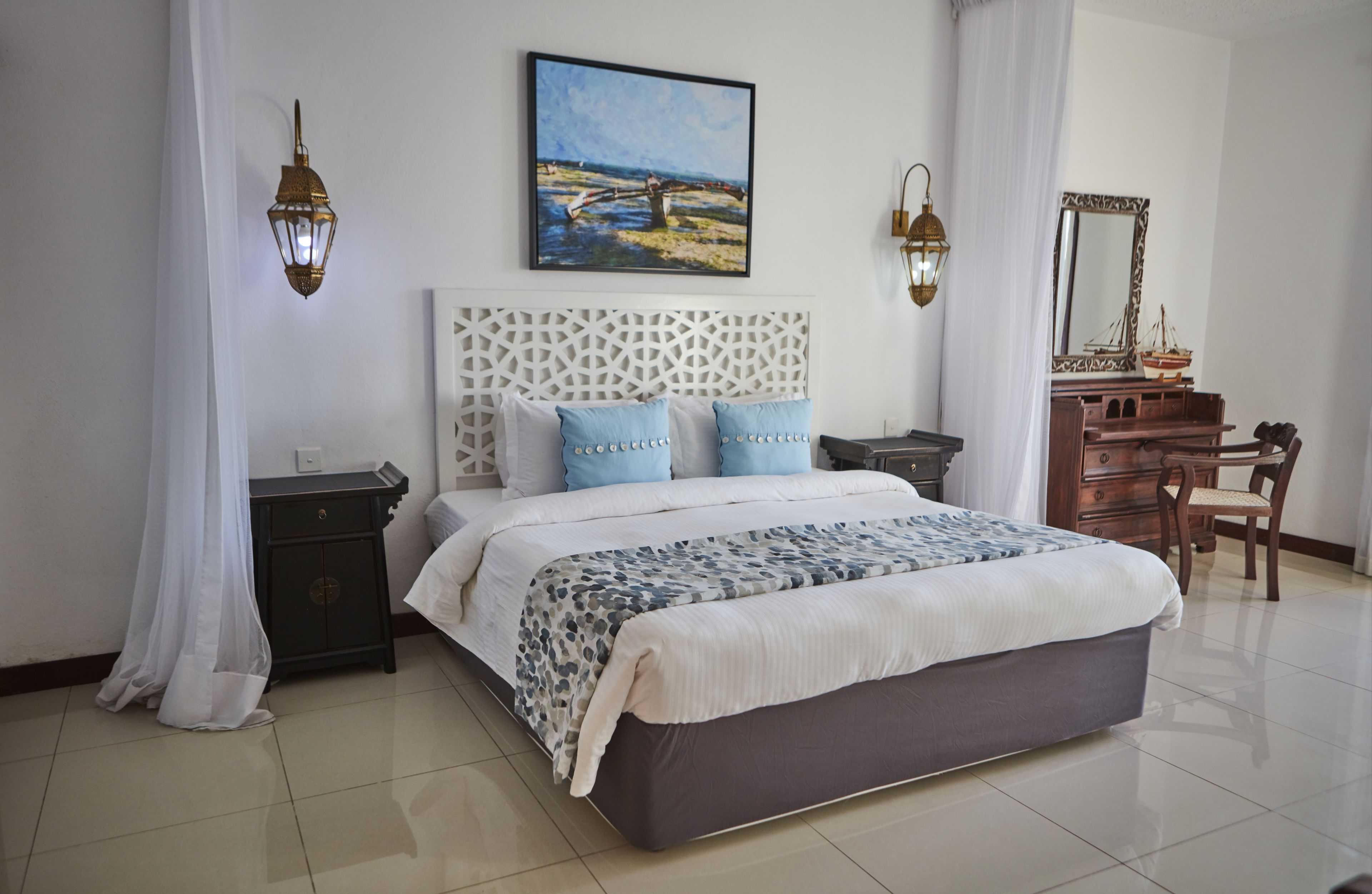 A neatly arranged bedroom with a large bed, a dresser, a chair, and a painting on the wall.