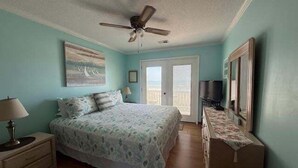 Un dormitorio con cama, ventilador de techo, televisor y puerta que da a un balcón.