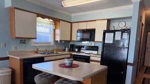 Una cocina compacta con una isla central, taburetes, un refrigerador y un microondas.
