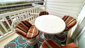 A balcony with a round table and four chairs, a view of the beach, and a white railing. - Boston Commons 102 3 Bedroom Condo by RedAwning (Surfside Beach)