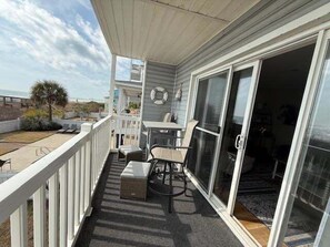 A covered outdoor area with a table and chairs, a sliding glass door, and a view of the outdoors. - Surfside By The Sea Ii 103 2 Bedroom Condo by RedAwning (Surfside Beach)