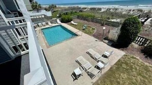 A pool with a view of the ocean, a grassy area with lounge chairs, and a stone wall.