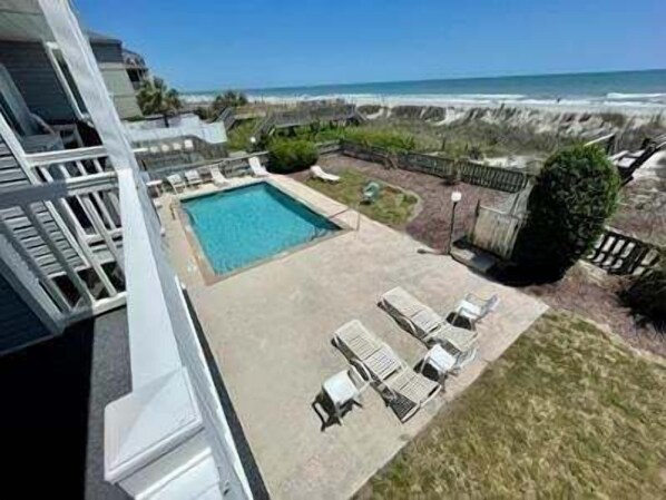 A pool with a view of the ocean, a grassy area with lounge chairs, and a stone wall.