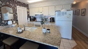 A kitchen with a granite countertop, white cabinets, a refrigerator, and a potted plant.