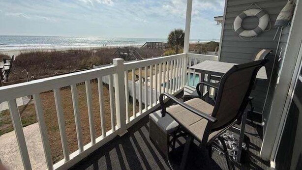 A covered porch with a view of the beach, a table, and a chair.