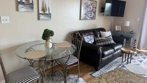 A living room with a glass table, black leather sofa, and artwork on the walls.