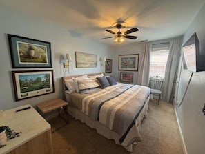 A bedroom with a bed, a nightstand, a ceiling fan, and framed pictures on the walls.