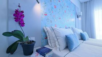 Quarto de hotel moderno com cama, mesa de cabeceira, planta em vaso e parede com papel de parede floral.