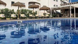A swimming pool with lounge chairs and umbrellas, surrounded by a building with multiple balconies and a clear blue sky. - Agua Hotels Alvor Jardim (Portimão)