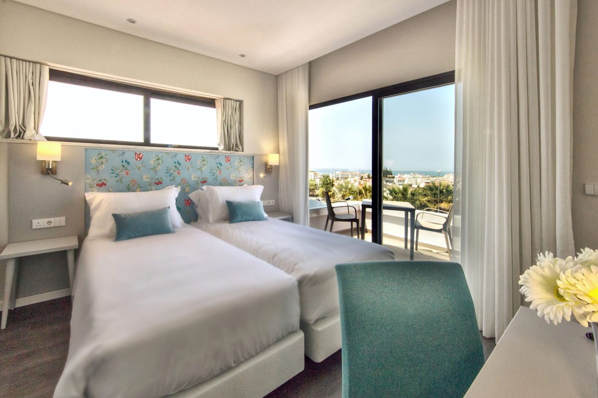 Une chambre d’hôtel avec deux lits, un bureau, une chaise et une vue sur la ville.