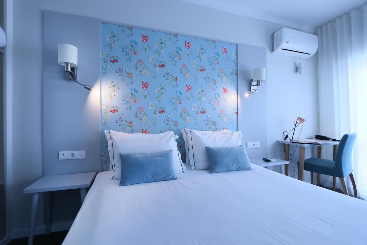 Une chambre d’hôtel avec un grand lit, deux tables de chevet, un bureau avec une chaise et un papier peint à motifs floraux.