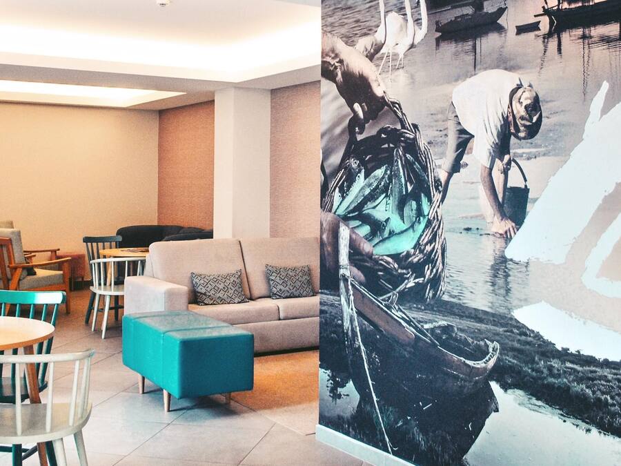 A modern interior with a sofa, teal ottoman, and dining area with chairs and tables.