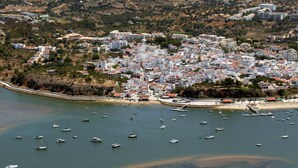 An aerial view of a coastal town with a marina filled with boats, surrounded by residential buildings and a sandy beach. - Agua Hotels Alvor Jardim (Portimão)