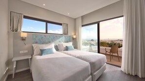 A hotel room with two beds, a small desk, a window with curtains, and a balcony with a chair. - Agua Hotels Alvor Jardim (Portimão)