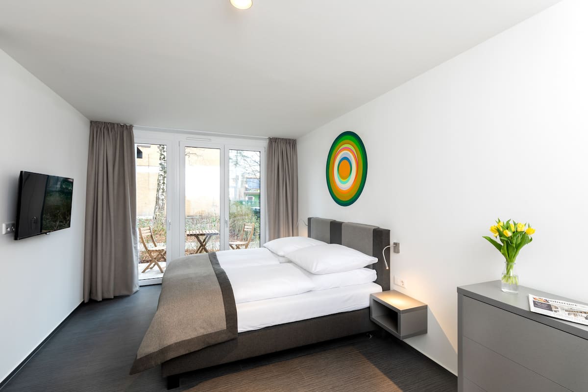 Una habitación de hotel moderna con una cama grande, un televisor de pantalla plana, un escritorio con un florero y una pieza de arte colorido en la pared.
