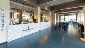 Amplio espacio interior con una recepción identificada como “Boardinghouse St. Pauli”, con un diseño moderno que incluye techos de hormigón visto y lámparas colgantes.