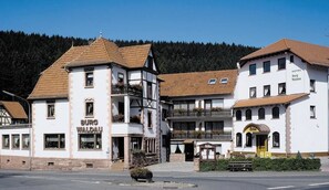 Een traditioneel gebouw met een bordje 'Burg Waldau', wat een hotel aangeeft. Het heeft een balkon met leuningen en een kleine ingang met een luifel.