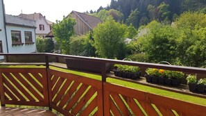 A balcony with a wooden railing, potted plants, and a view of a residential area with houses and trees. - Hotel Burg Waldau (Grasellenbach)