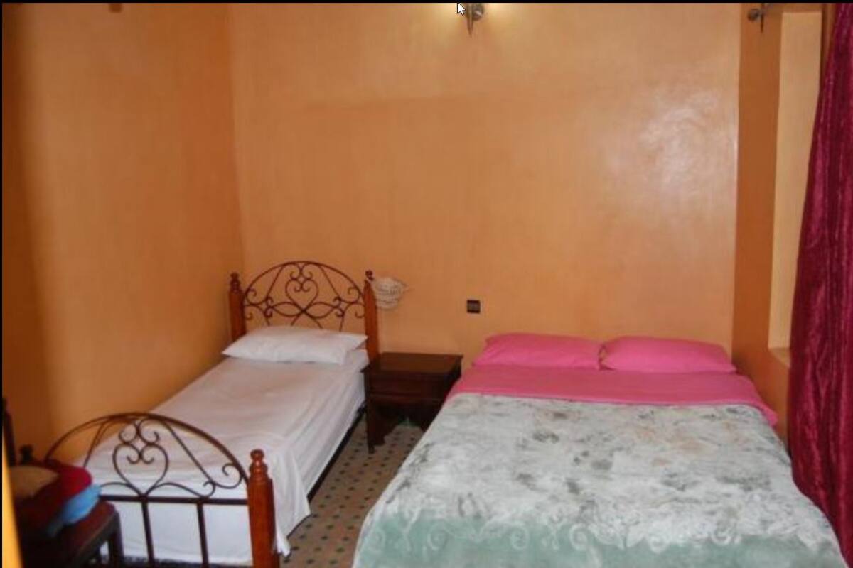 A small bedroom with two beds, one with a metal frame and the other with a wooden frame.