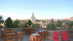 Eine Terrasse mit Tischen und Stühlen, Blick auf eine Moschee und eine Stadtkulisse im Hintergrund.