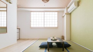 A minimalist room with tatami flooring, a low table with cushions, and a large window providing natural light. - Guest House MIYABI (Kyoto)