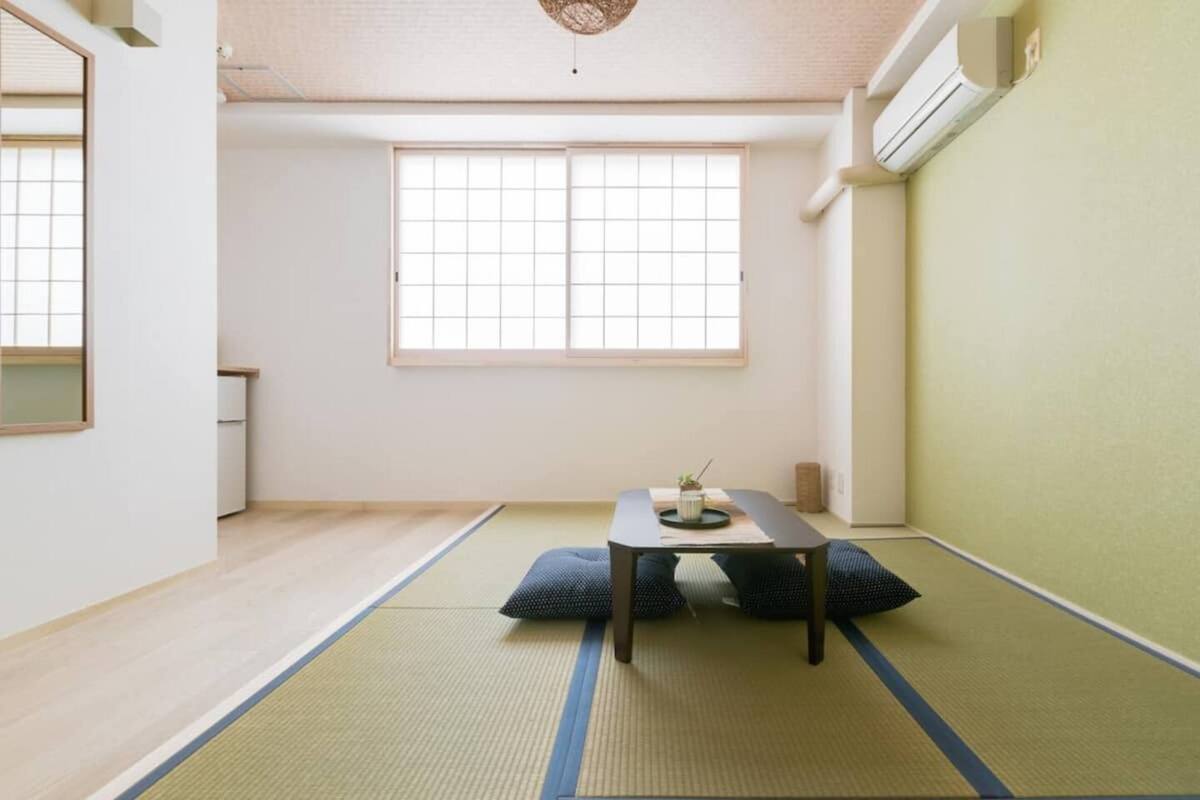 Quarto minimalista com piso de tatame, mesa baixa com almofadas e uma grande janela que proporciona iluminação natural.