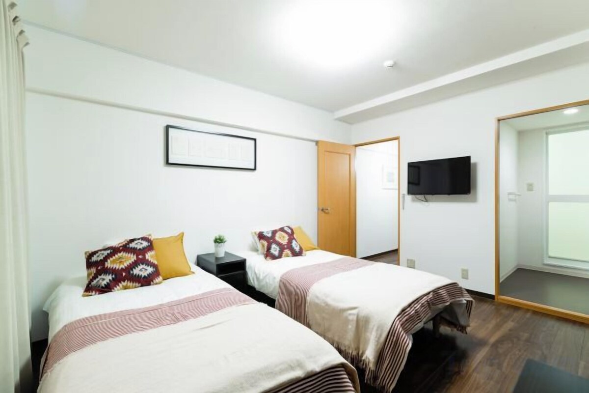 Habitación de hotel con dos camas, un televisor y una puerta que da a un baño.