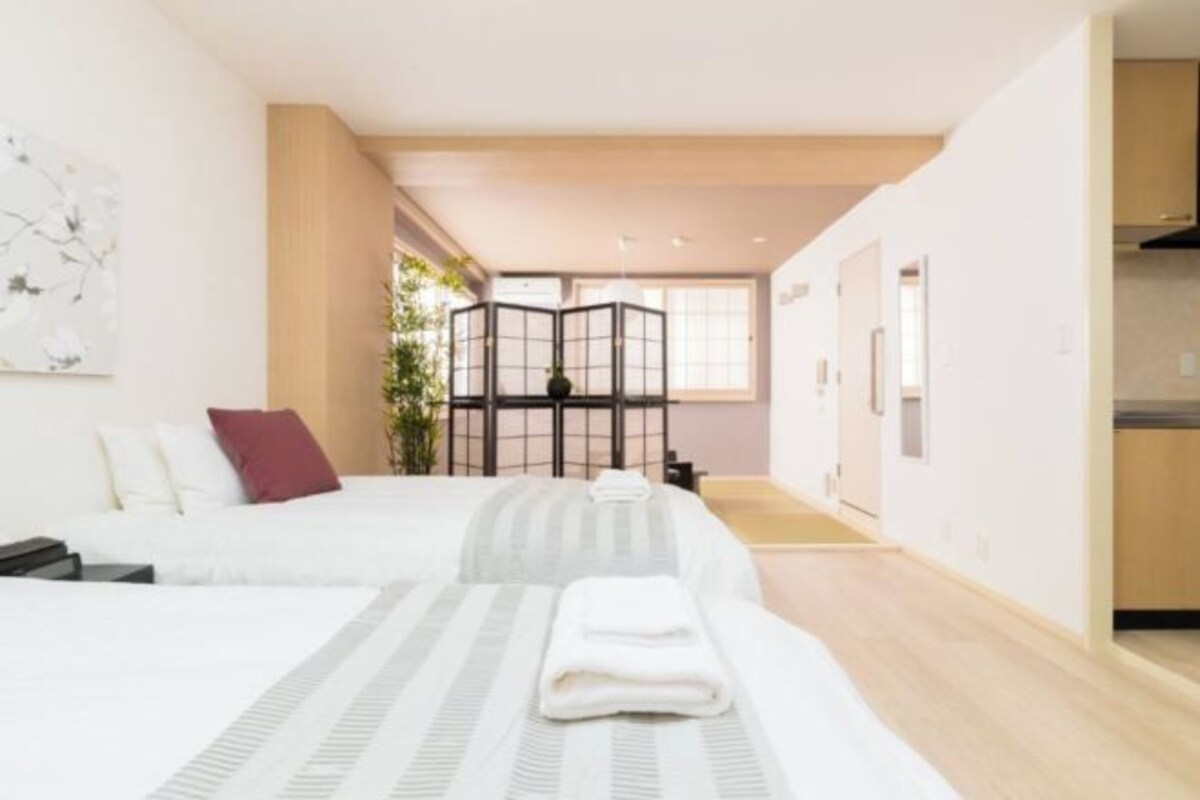 Camera d'albergo moderna con due letti, un'ampia finestra, angolo cottura e una porta scorrevole che dà su un balcone.