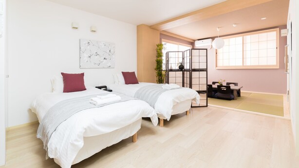 A modern hotel room with two beds, a dining area, and a large window providing natural light. - Guest House MIYABI (Kyoto)