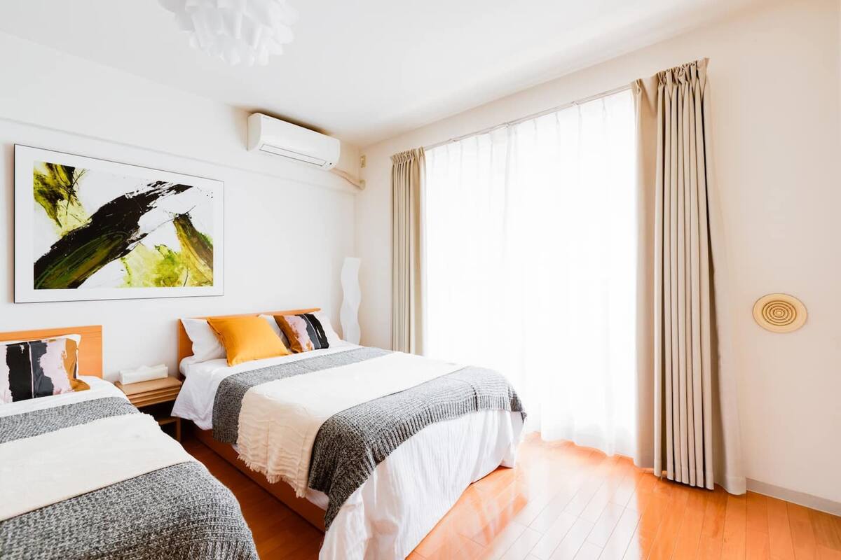 Quarto de hotel com duas camas, uma janela grande com cortinas, ar-condicionado fixado na parede e um quadro.