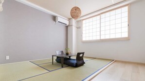 A room with tatami mat flooring, a low table with chairs, a hanging light fixture, and a large window with a grid pattern. - Guest House MIYABI (Kyoto)