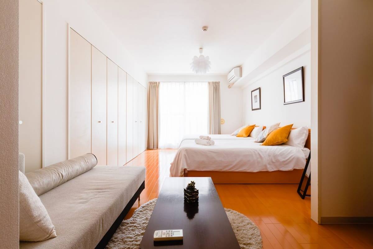Quarto de hotel moderno com sofá, duas camas, mesa de centro e uma janela grande.