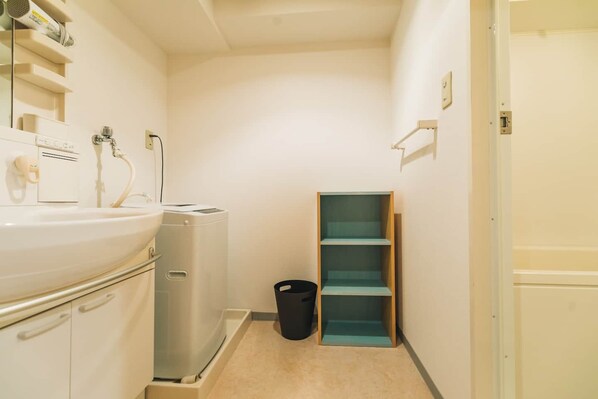 A small bathroom with a sink, a hairdryer, a washing machine, and a trash bin. - Guest House MIYABI (Kyoto)