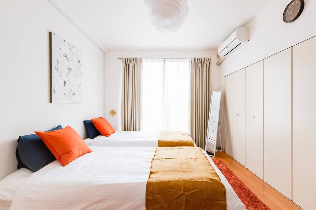 Quarto de hotel com duas camas, uma janela grande com cortinas, um guarda-roupa e um ar condicionado fixado na parede.