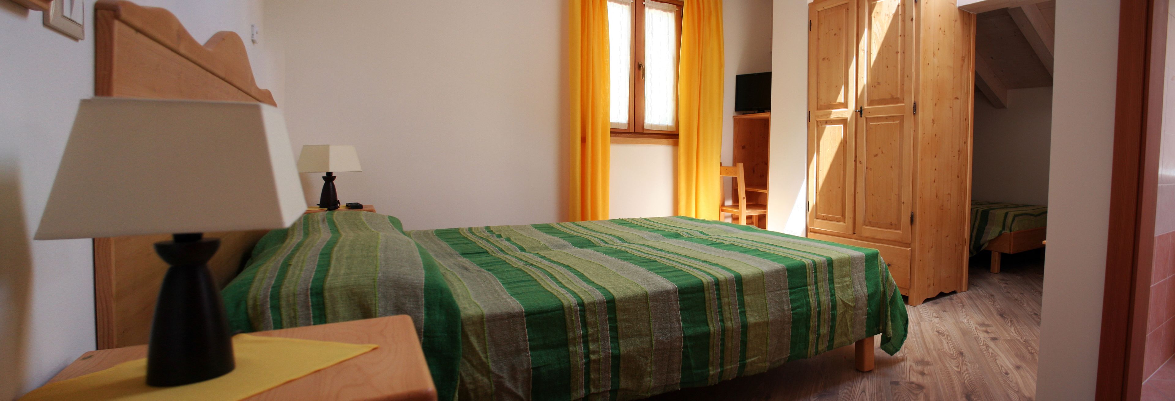 Una stanza con un letto ricoperto da lenzuola a righe verdi, un comodino con una lampada e un armadio in legno.