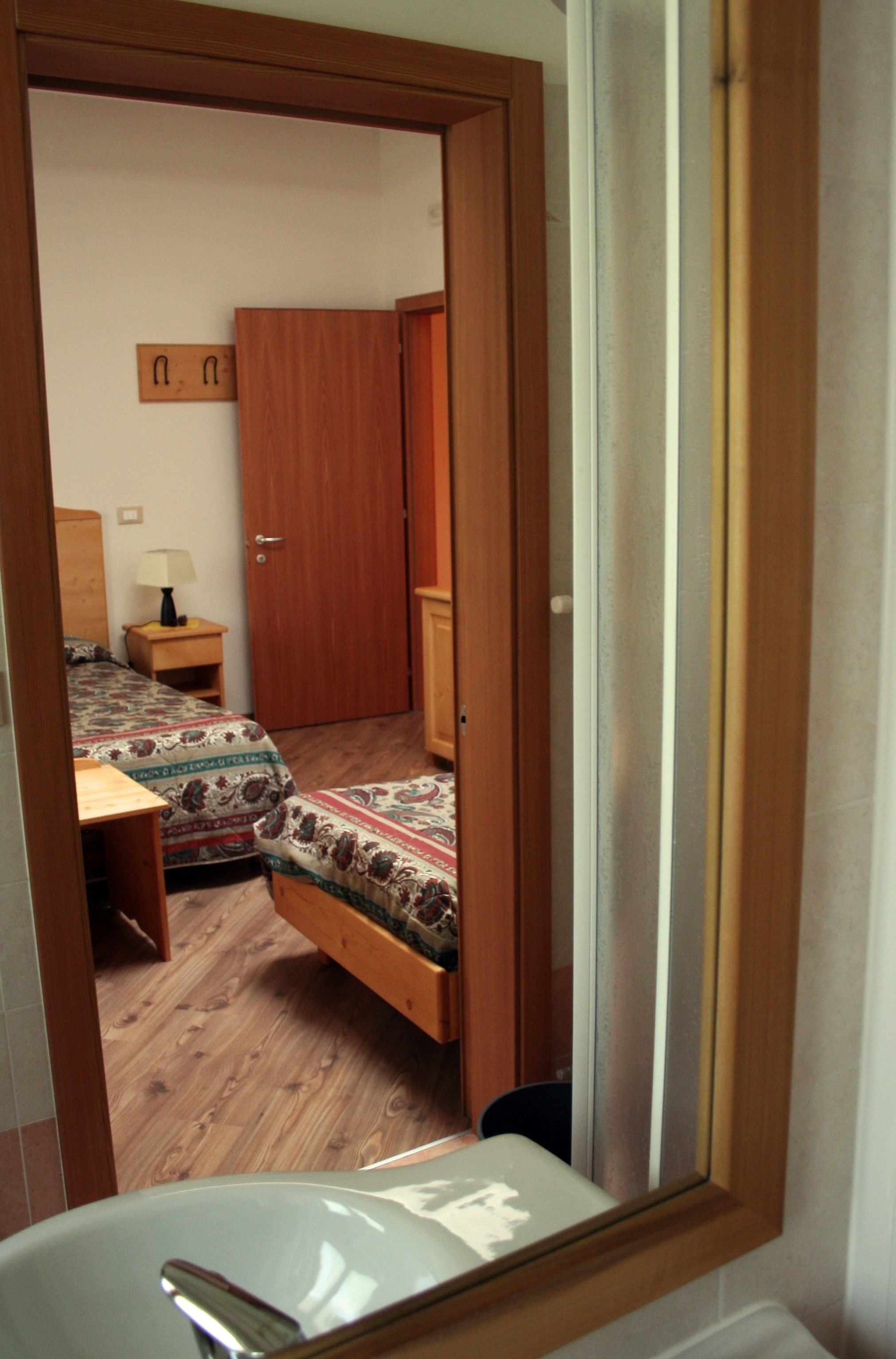 Una camera da letto con due letti singoli, un armadio in legno, un comodino con una lampada e un bagno con lavandino e specchio.