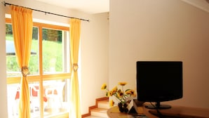 A room with a wooden desk, a black monitor, and a window with yellow curtains. - Garnì Sella al Cipriani (Borgo Valsugana)