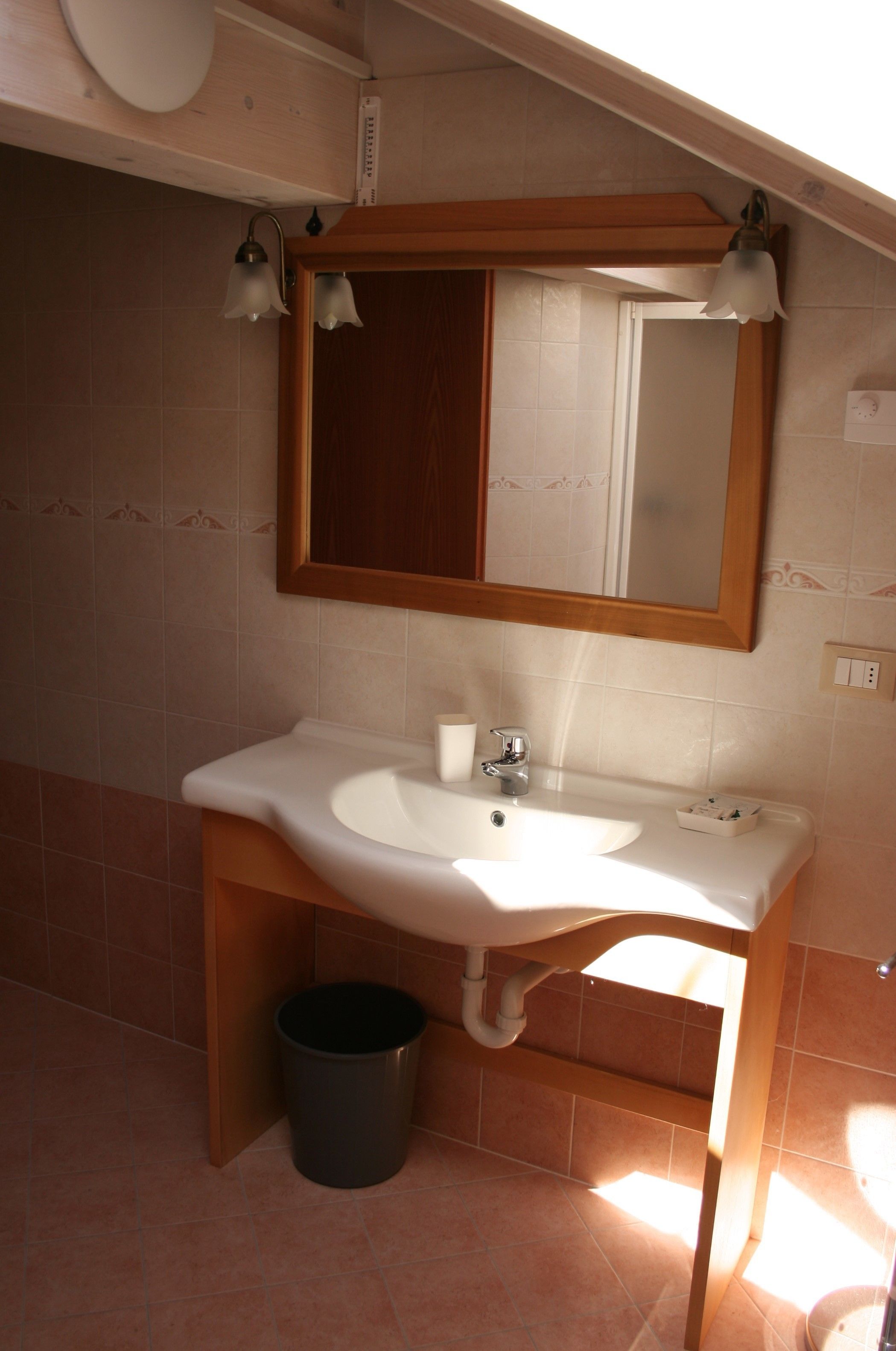 A bathroom with a white sink, a mirror, and a trash can.