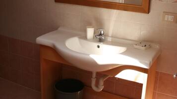 A bathroom with a white sink, a mirror, and a trash can.