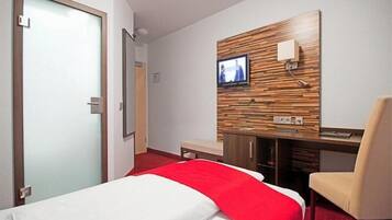 Una habitación de hotel con cama, escritorio, silla y televisor en la pared.