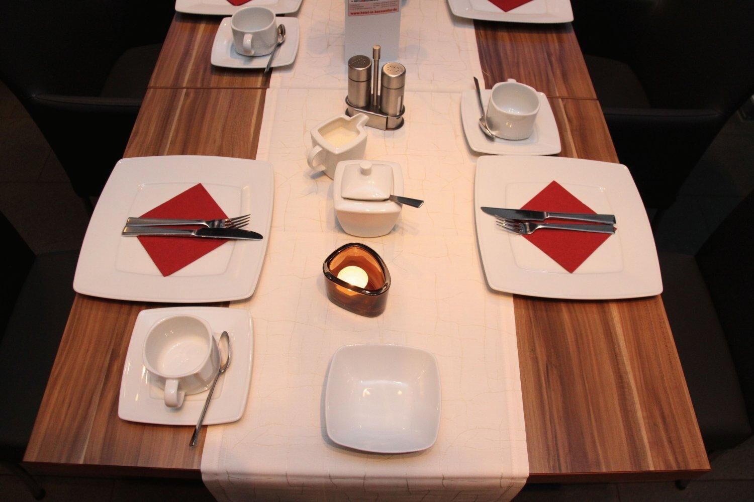 A neatly set dining table with white plates, red napkins, and silverware.