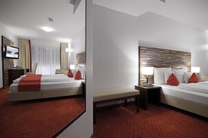 Una habitación de hotel con cama, una banca, una mesita de noche, un televisor y una ventana con cortinas.